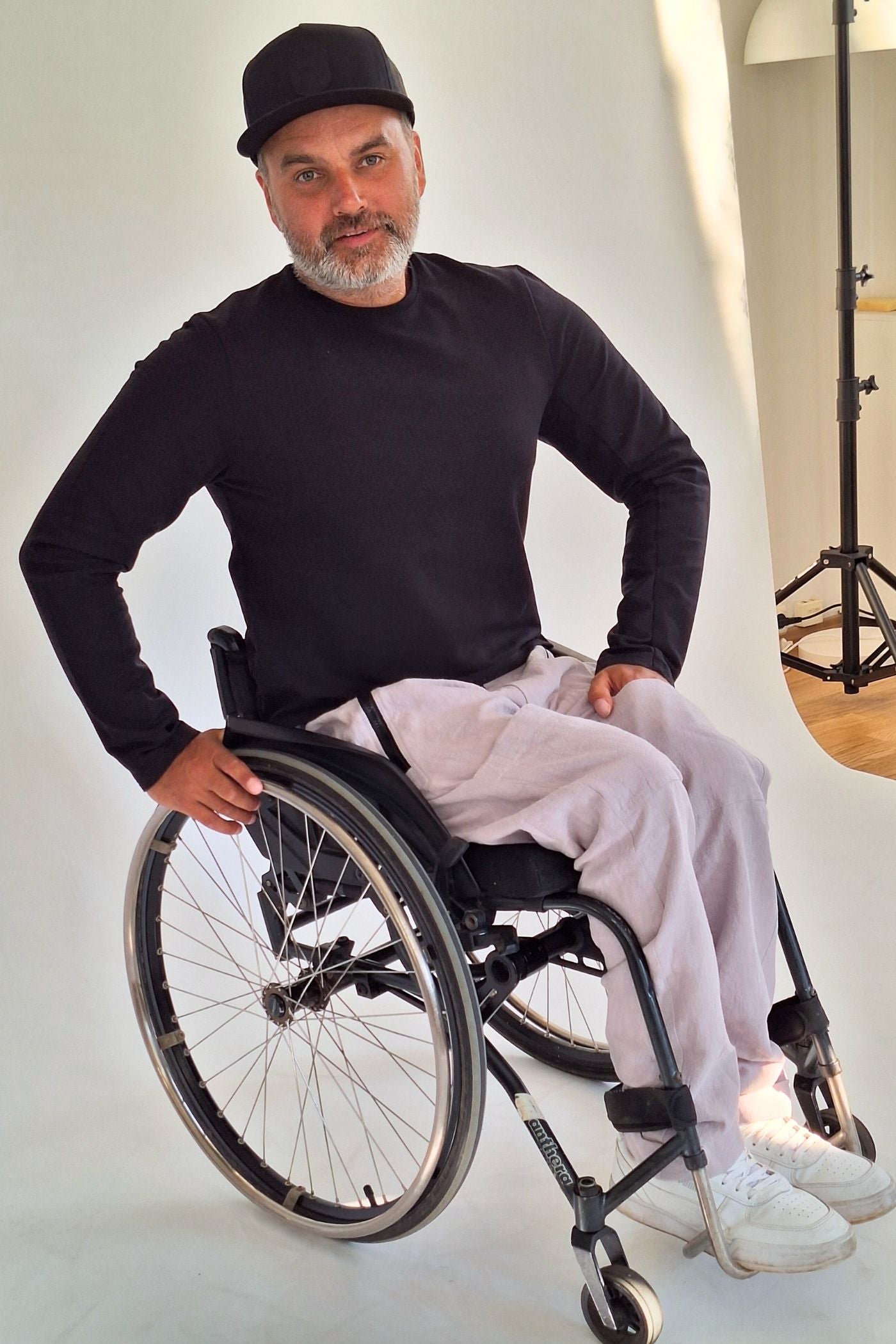 Mann im Rollstuhl trägt bequeme Sommerrollstuhlhose und ein schwarzes Oberteil. Die adaptive Bekleidung von Vilber's ist speziell für Behinderte konzipiert.